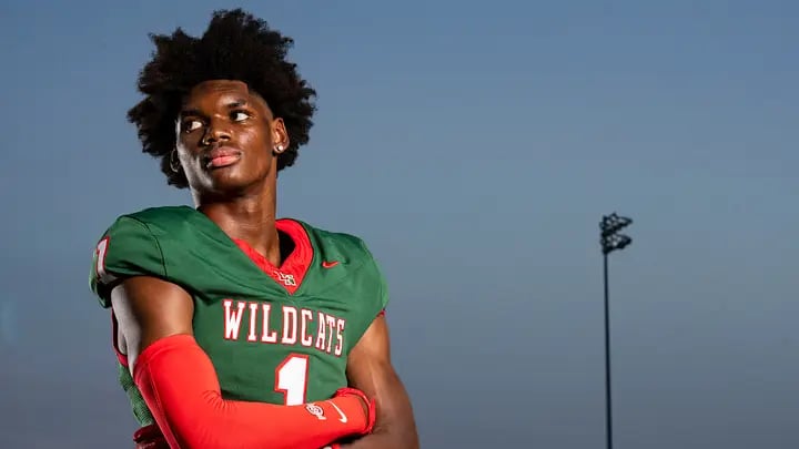 Lawrence North five-star wide receiver Monshun Sales in his green and red Wildcats number 1 uniform, arms crossed on the field at dusk.