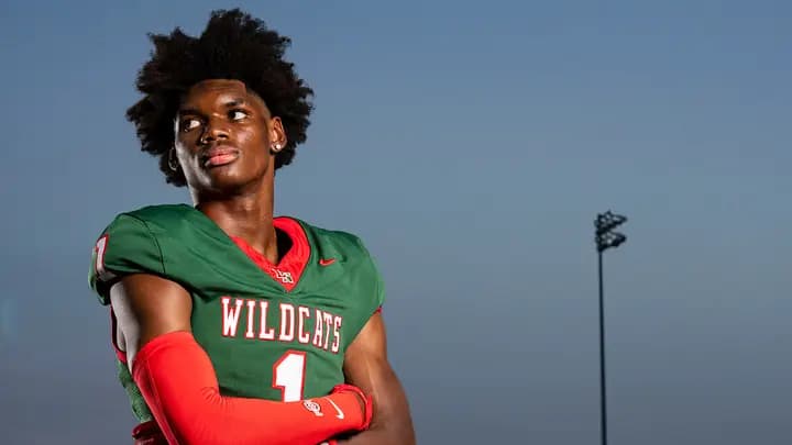 Lawrence North five-star wide receiver Monshun Sales in his green and red Wildcats number 1 uniform, arms crossed on the field at dusk.