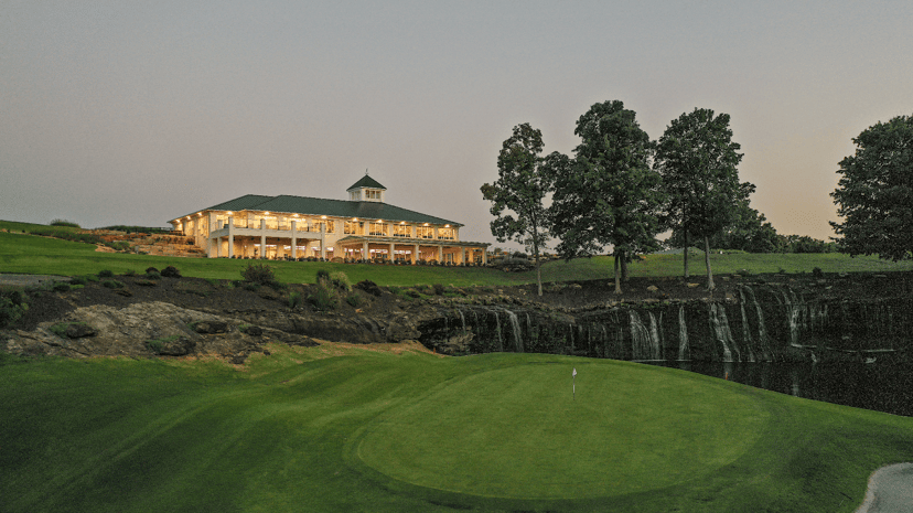 The 18th green and waterfall at Sultan's Run with the clubhouse lit at dusk