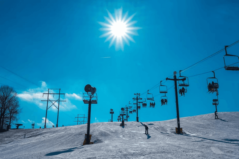 A chairlift climbing a snowy slope under bright blue skies at an Indiana ski resort