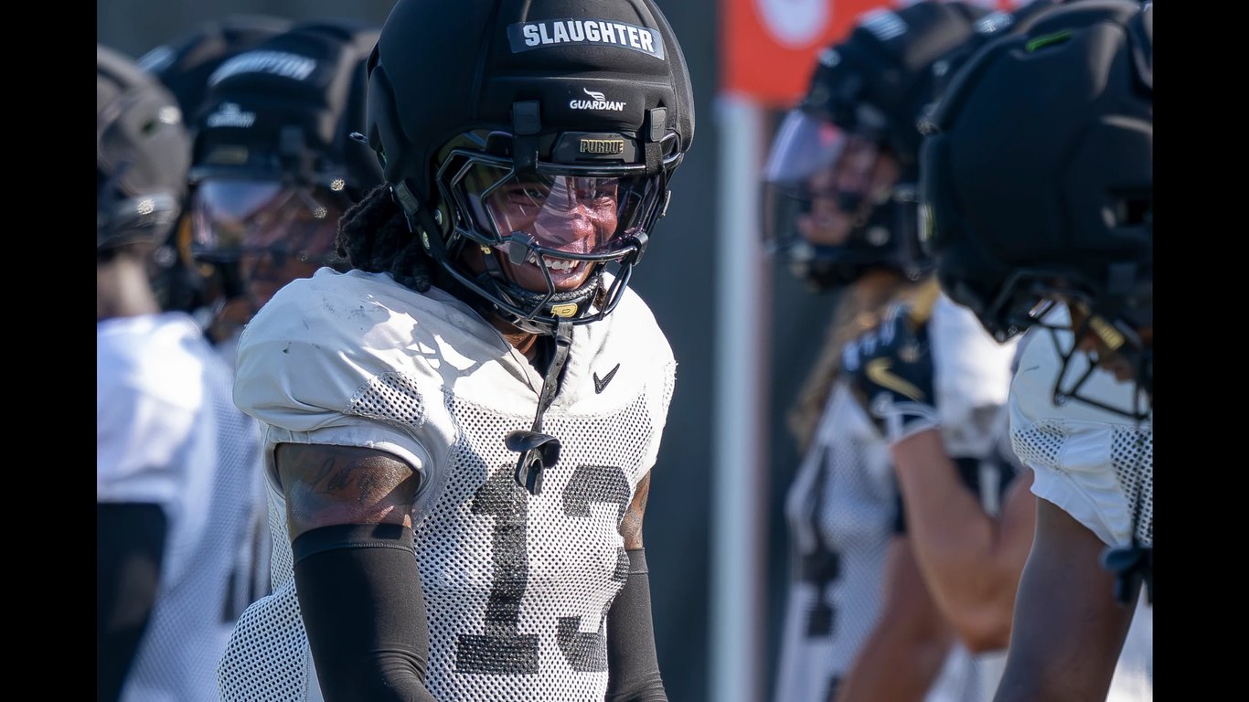 Purdue defensive back John Slaughter, in a black helmet with SLAUGHTER on the bumper and a white practice jersey, grins while lining up with teammates during fall camp.