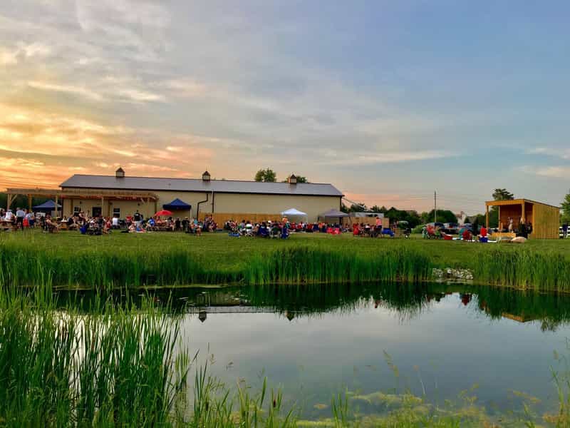 Barn and pond at sunset with a crowd on the lawn at Urban Vines Winery & Restaurant in Westfield