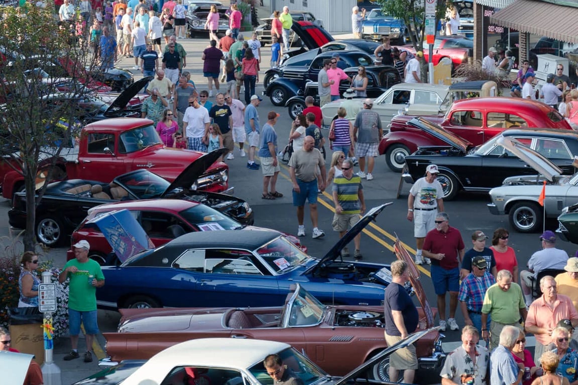 Crowds walk among rows of classic cars with open hoods at the Downtown Cruise-In in Auburn, Indiana