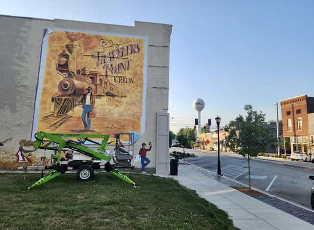 The 'Travelers Point' vintage train mural painted on a brick building along Main Street in downtown Kirklin, Indiana, with the town water tower in the background.