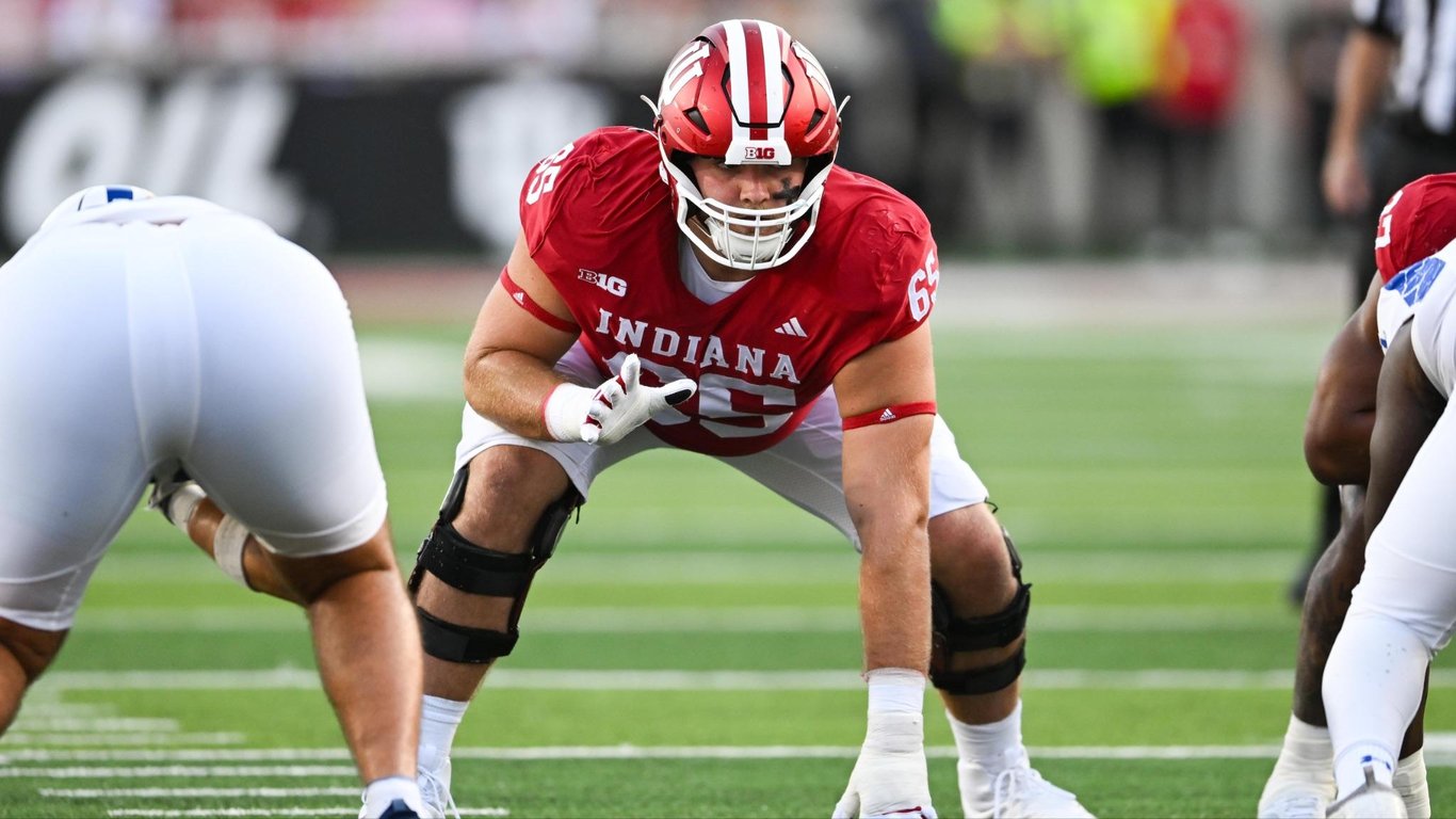 Indiana offensive lineman in a crimson No. 65 jersey sets in his stance at the line of scrimmage during a home game