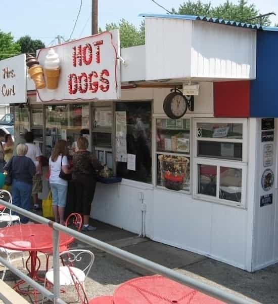 Walk-up window with the Hot Dogs sign and red patio tables at Mrs. Curl Ice Cream Shop in Greenwood