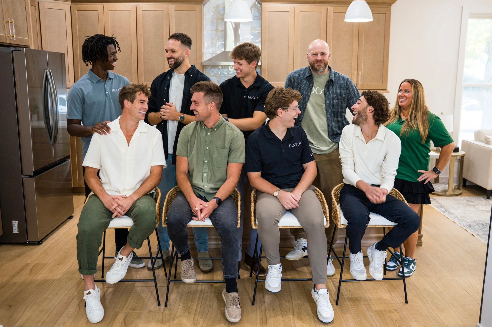 The Roots Realty team together in a kitchen, some seated and some standing behind