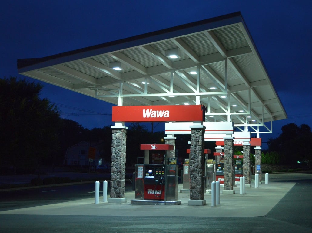 A Wawa fuel canopy lit up at night, with stone-faced columns and a red Wawa sign over the pumps