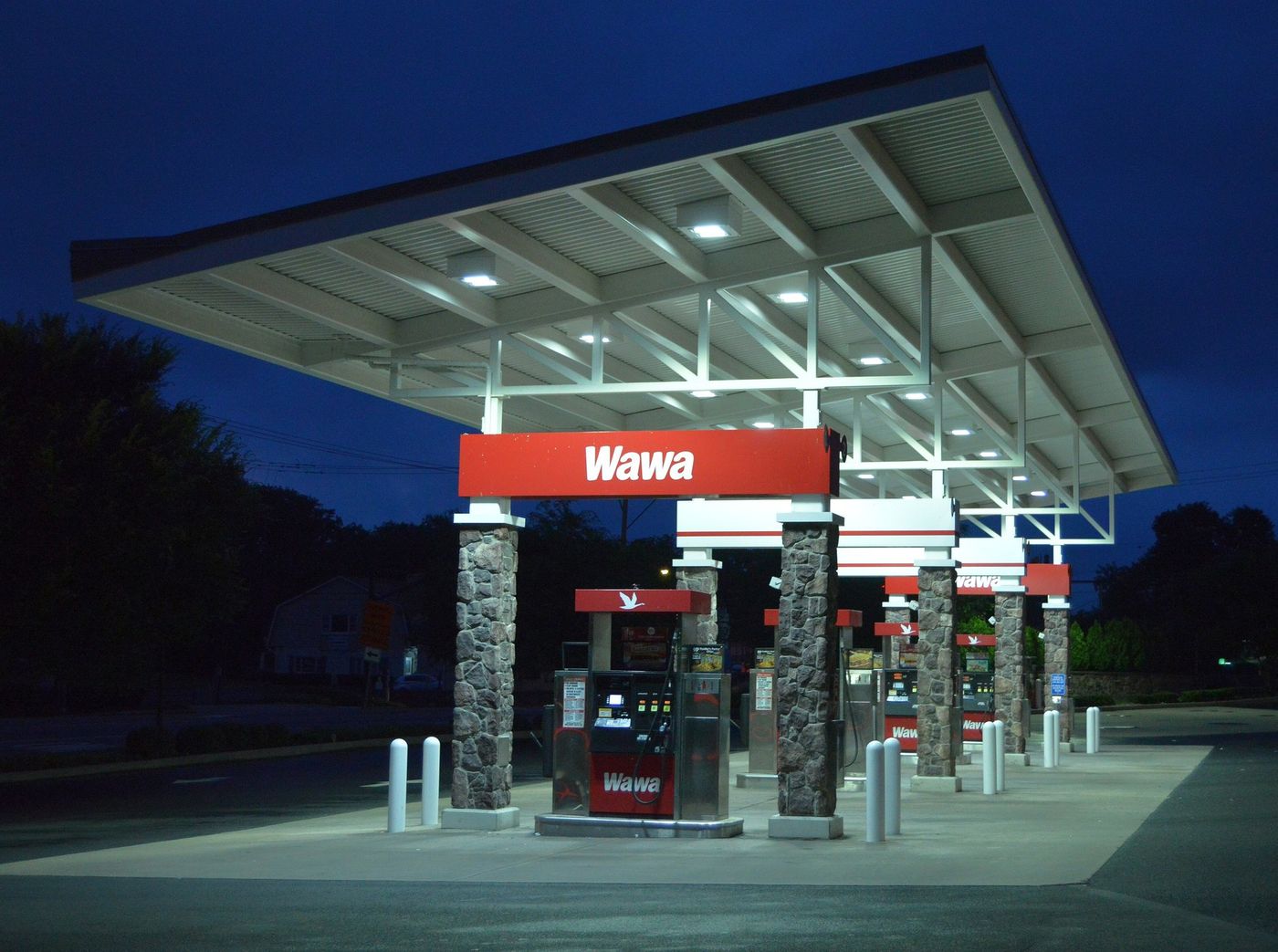 A Wawa gas station canopy lit at night, with a red Wawa sign above fuel pumps and stone-faced support columns
