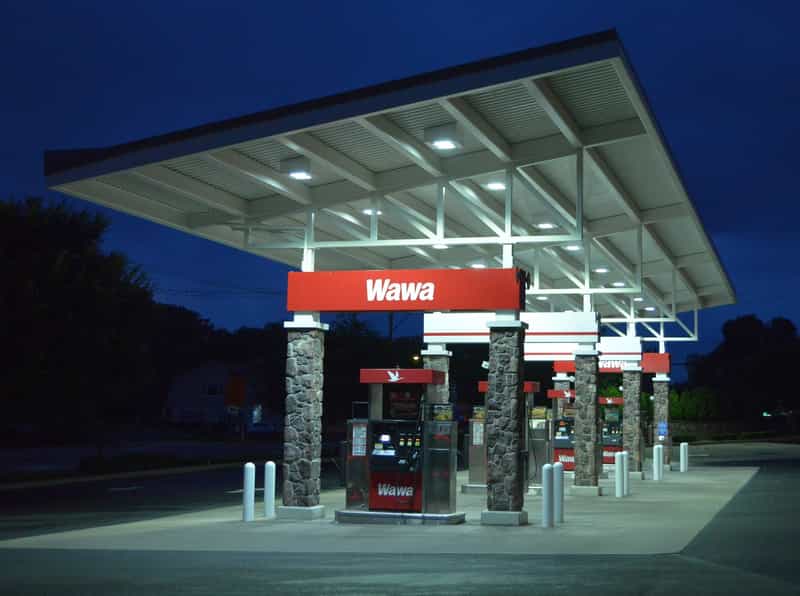 A Wawa gas station canopy lit at night, with a red Wawa sign above fuel pumps and stone-faced support columns