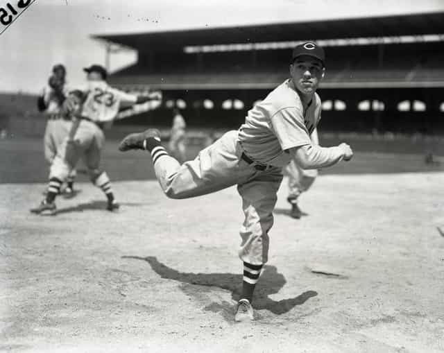 Vintage black-and-white photo of a baseball pitcher in a Cleveland uniform following through on a pitch at a packed ballpark.