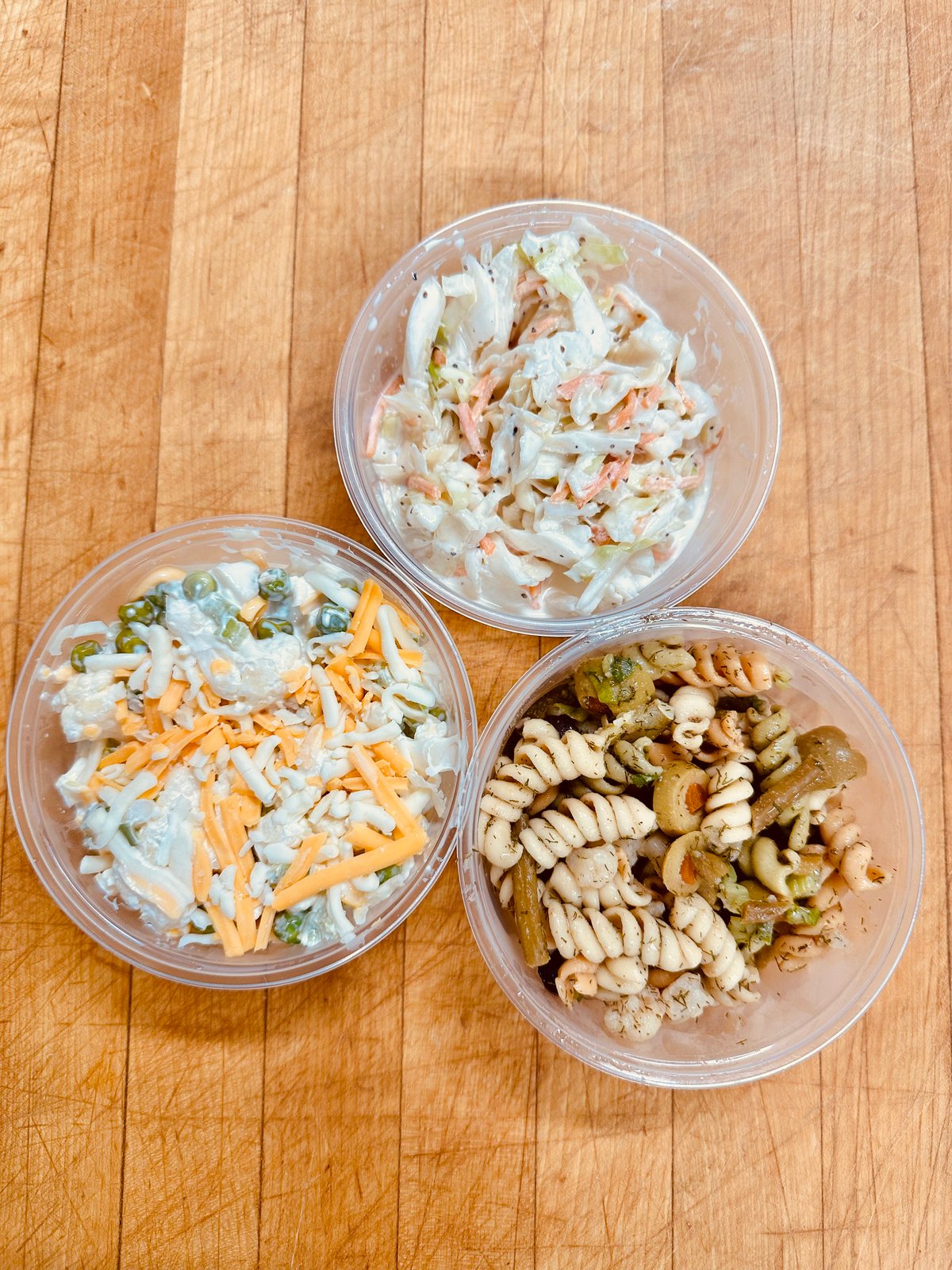 Deli salads by the pound at Illinois Street Food Emporium: coleslaw, pea salad, and pasta salad in takeaway containers.