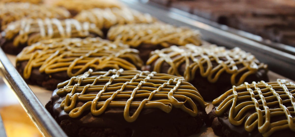 Chocolate cookies finished with a peanut butter drizzle, lined up on a tray in the bakery case