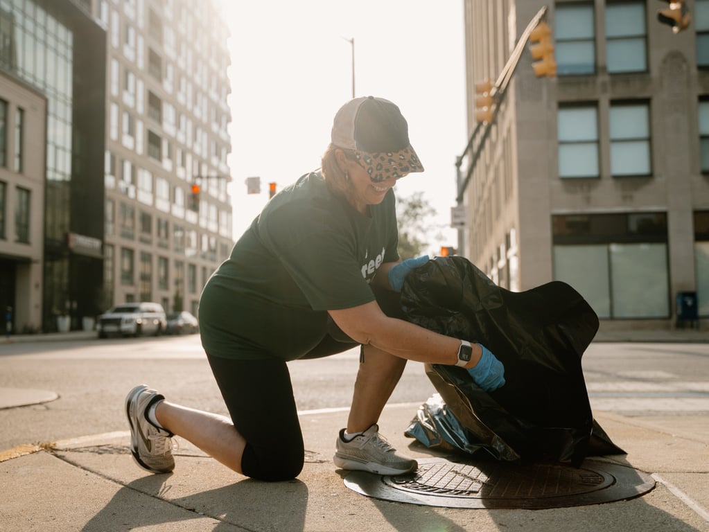 A volunteer bagging litter at a downtown corner in the early morning light