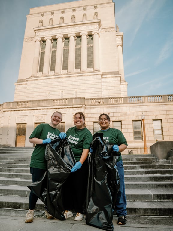 Three volunteers holding trash bags on the World War Memorial steps