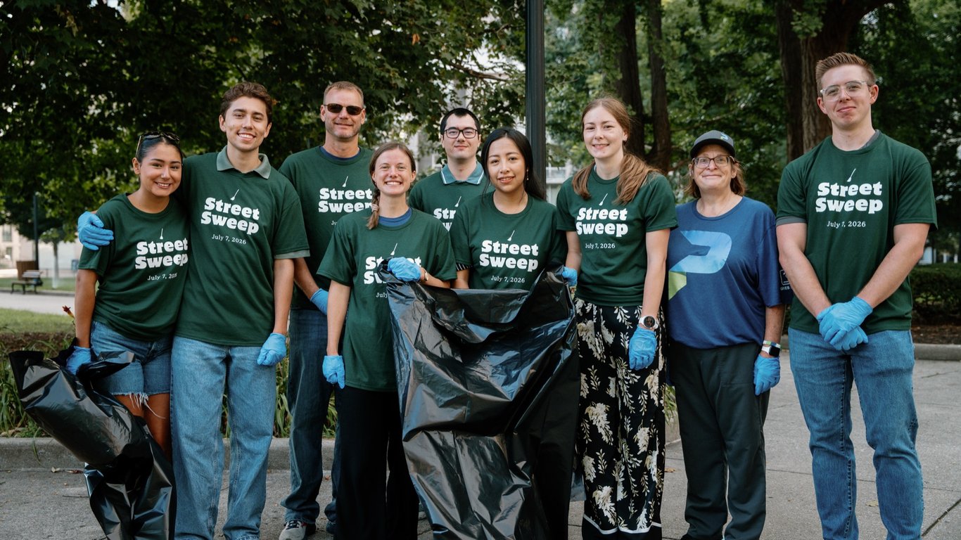 A crew of volunteers with a trash bag on a tree-lined downtown path