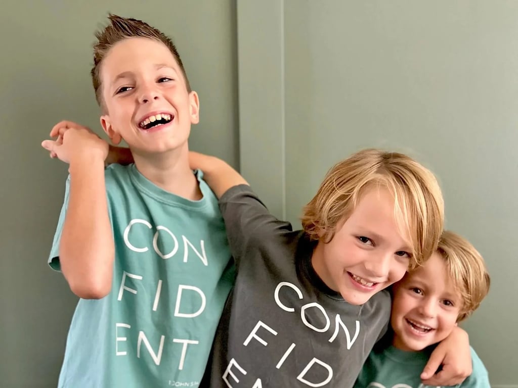Three boys in matching Little District shirts, arms around each other, laughing