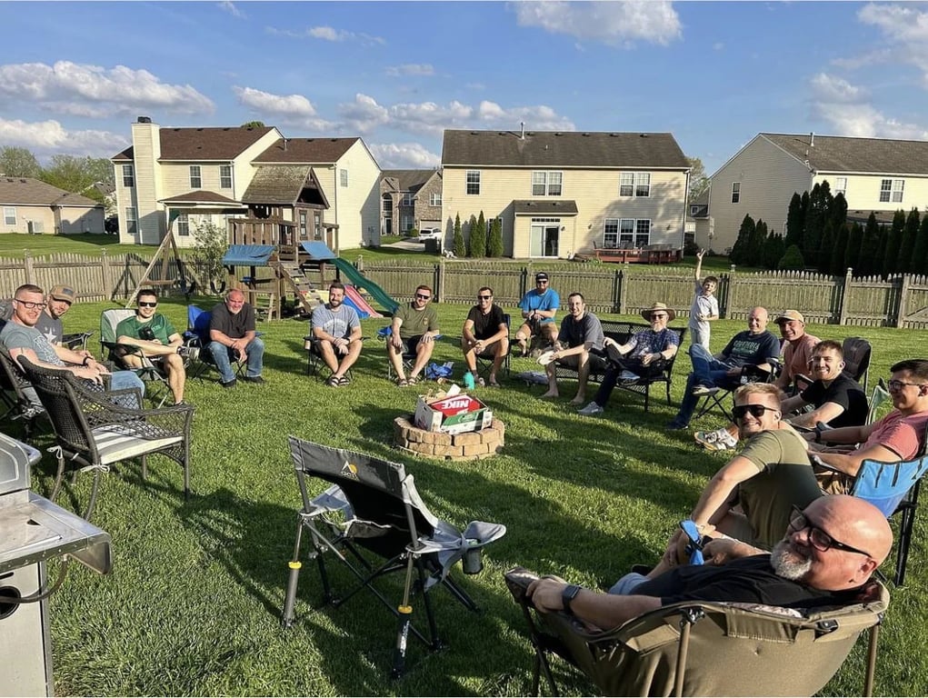 The men of The District Church sitting in a wide circle around a backyard fire pit