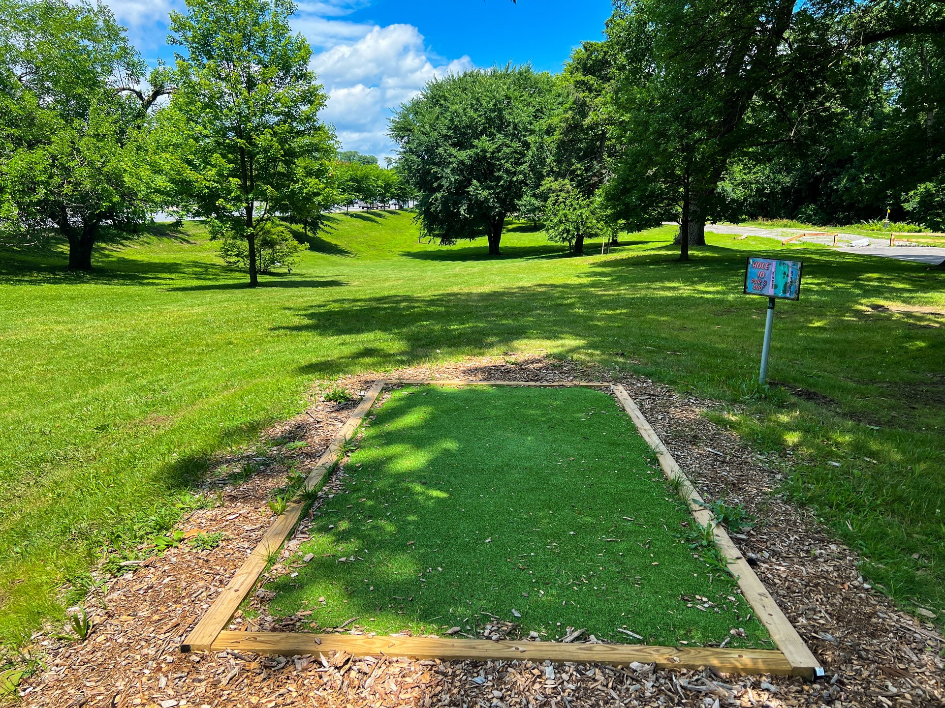 Hole 10's tee. Par 3. Pink basket is straight ahead through the trees and then slightly on the right, and is 309 ft. Road on both side is OB. Currently there is no Yellow Basket on Hole 10. 