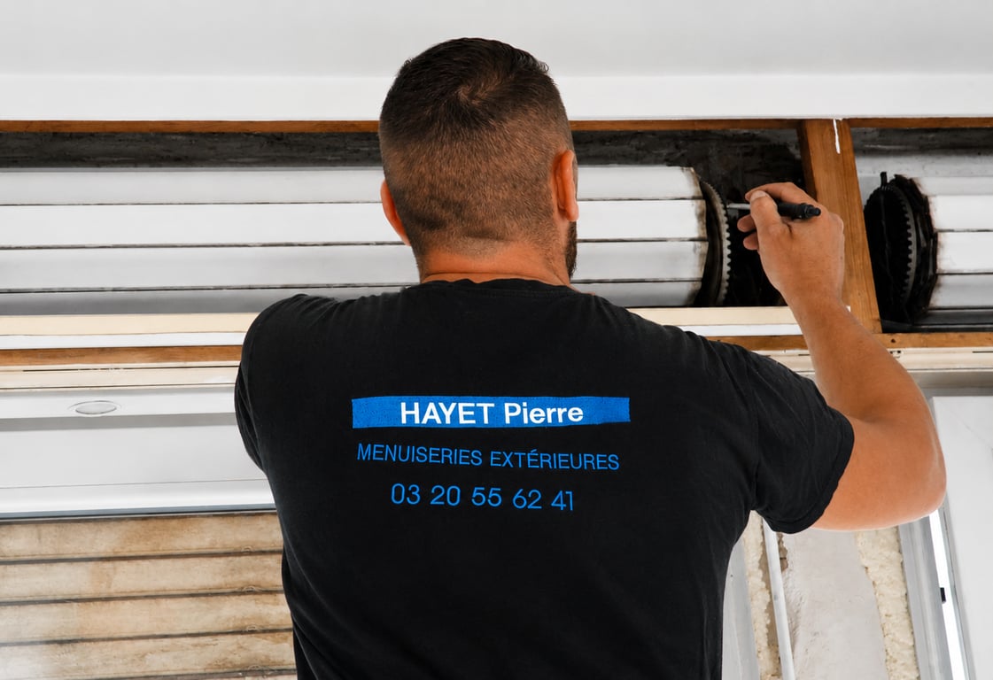 Un poseur intervenant dans le coffre d'un volet roulant, t-shirt siglé de dos