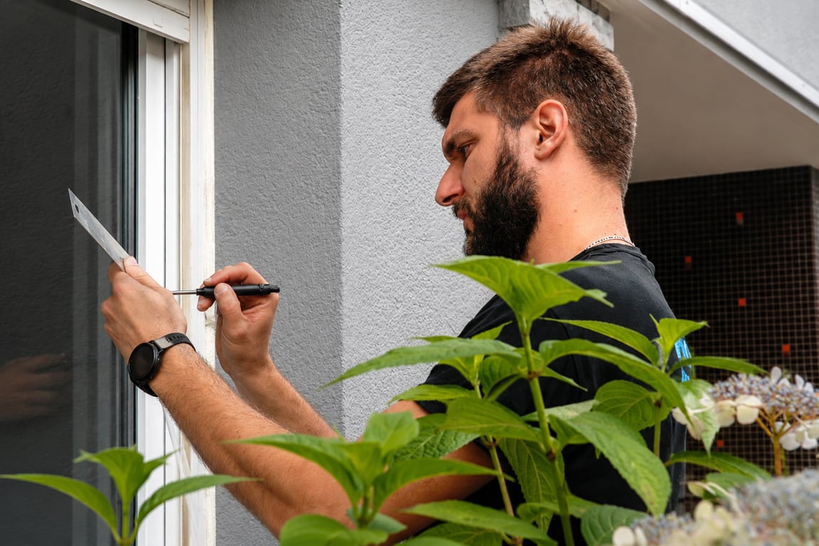 Un poseur de l'équipe vissant une patte de fixation sur le dormant d'une fenêtre
