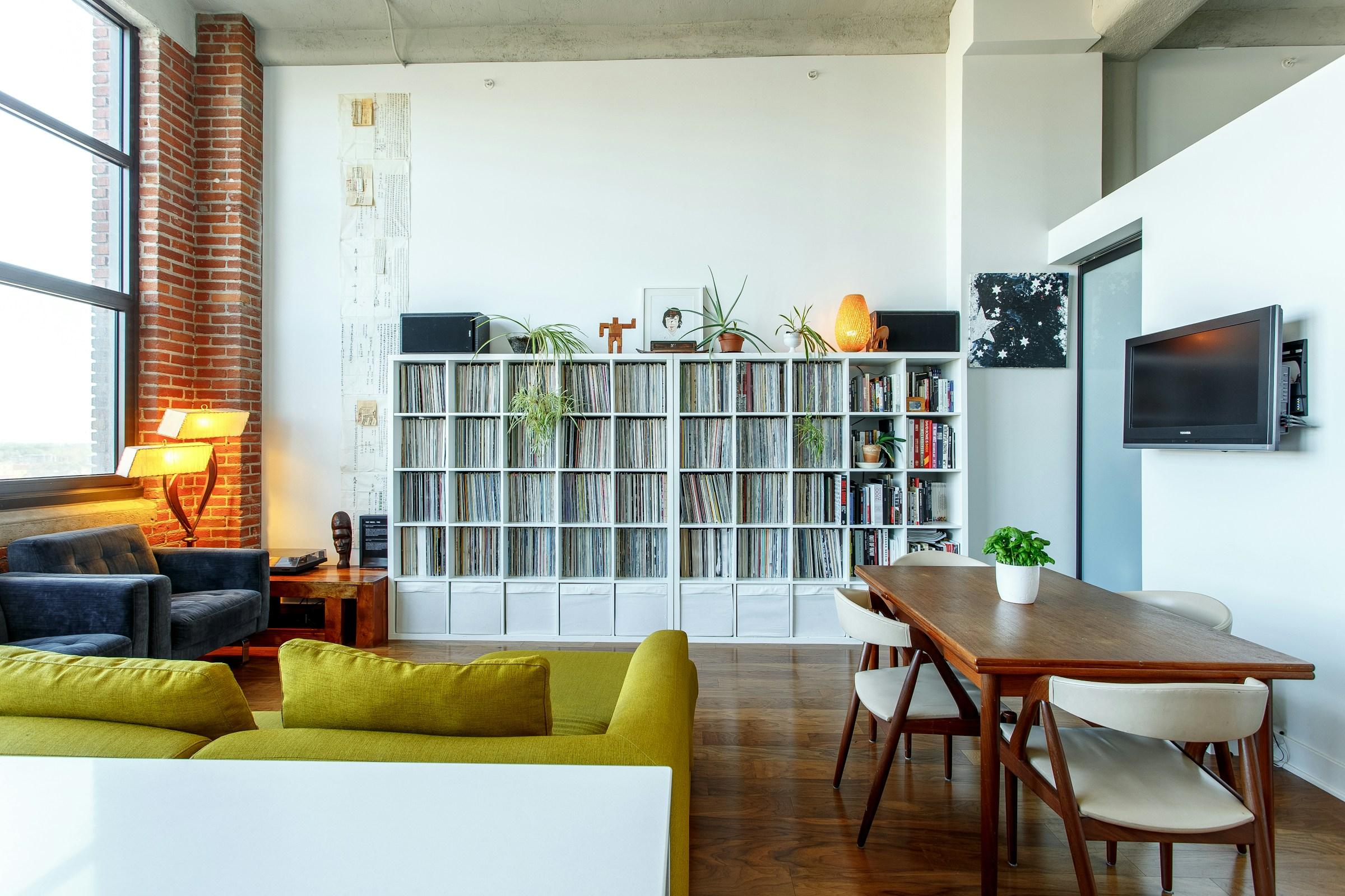 Séjour de loft au mur de brique apparente, bibliothèque blanche et table à manger.