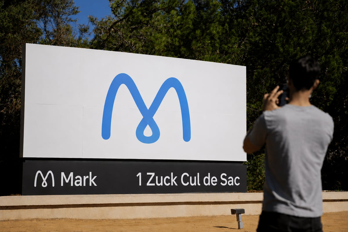 Person photographing a sign with a blue "M" logo and text "Mark 1 Zuck Cul de Sac" in a wooded area.