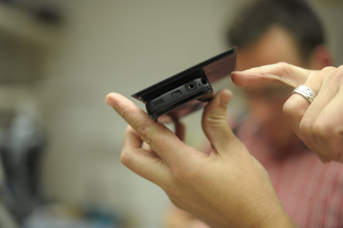 A person points to the edge of a Nokia N900 held against a thin plate, with the phone ports visible.