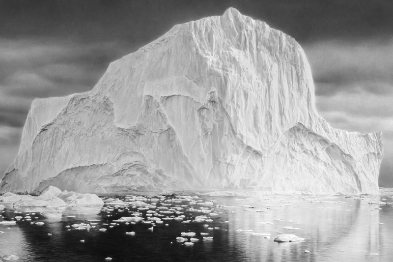 Large iceberg floating in calm water under a cloudy sky.