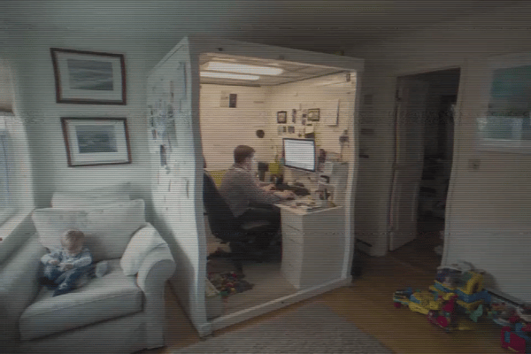 Home office with a person at a desk and a child sitting on a couch nearby.