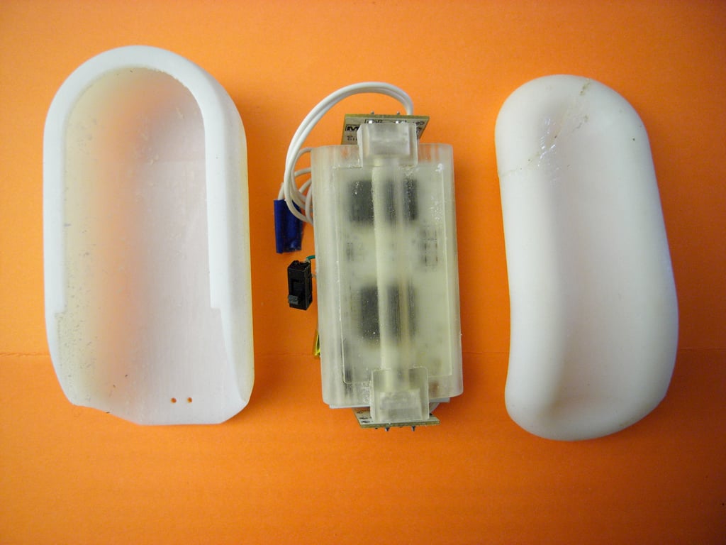 Kombolói disassembled into two white shell halves and a translucent internal assembly on an orange surface, with a crack visible in the right shell.