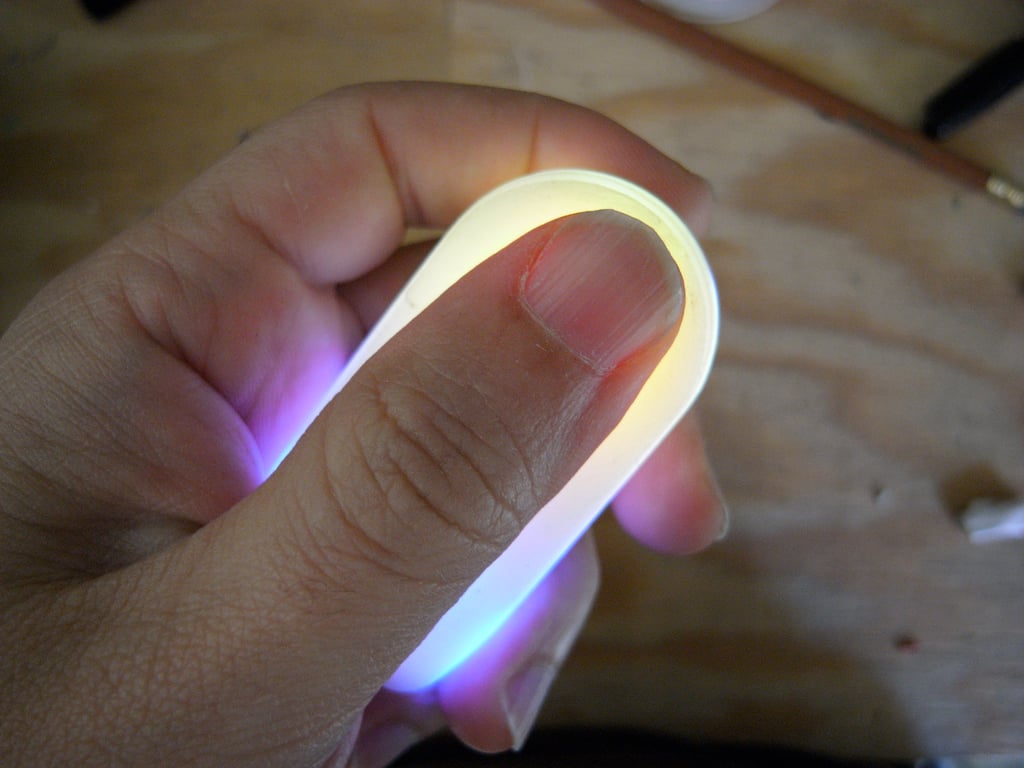 A thumb resting along Kombolói as its rounded upper end glows yellow and its lower end glows blue.