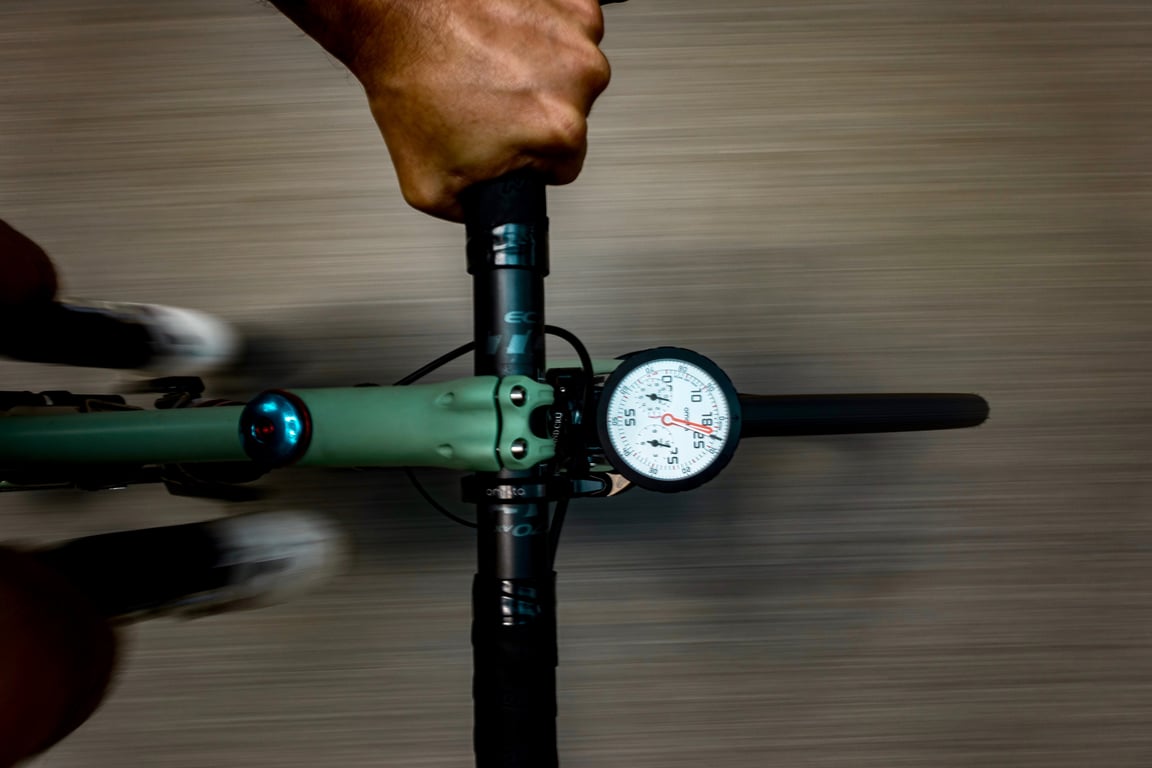 Looking down at the OMATA One mounted on green bicycle handlebars while the road blurs underneath.