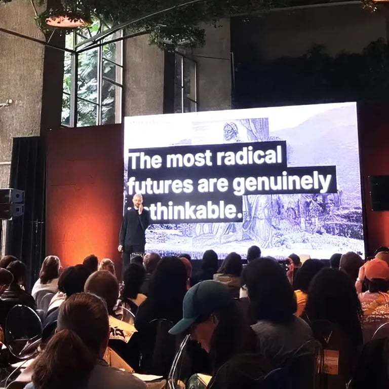 A talk being given to a packed audience with the phrase 'The most radical futures are genuinely unattainable' on the screen