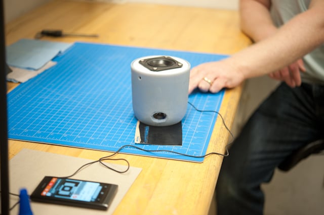White Social Speaker prototype on a blue cutting mat beside a phone during testing.