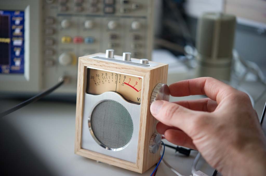 Hand adjusting a knob on a wood-framed radio prototype with an analog meter.