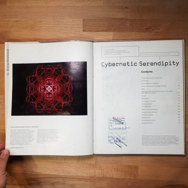 Open book on a wooden table, showing a
colorful geometric design on the left and “Cybernetic Serendipity” contents on the right.
