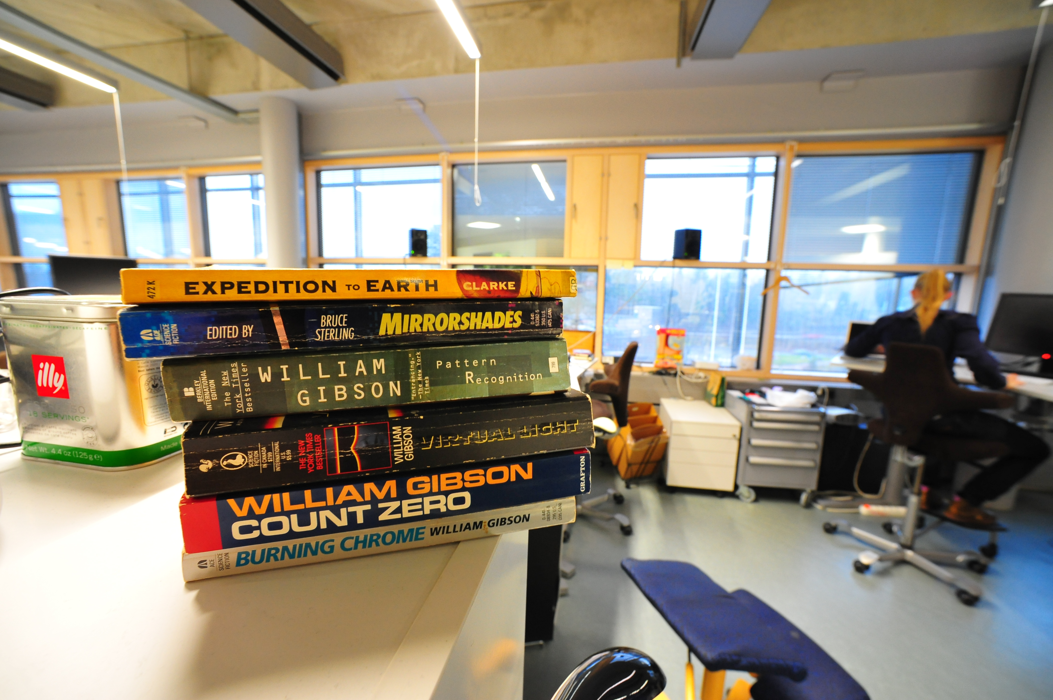 Science-fiction books by William Gibson and other authors stacked beside a desk.