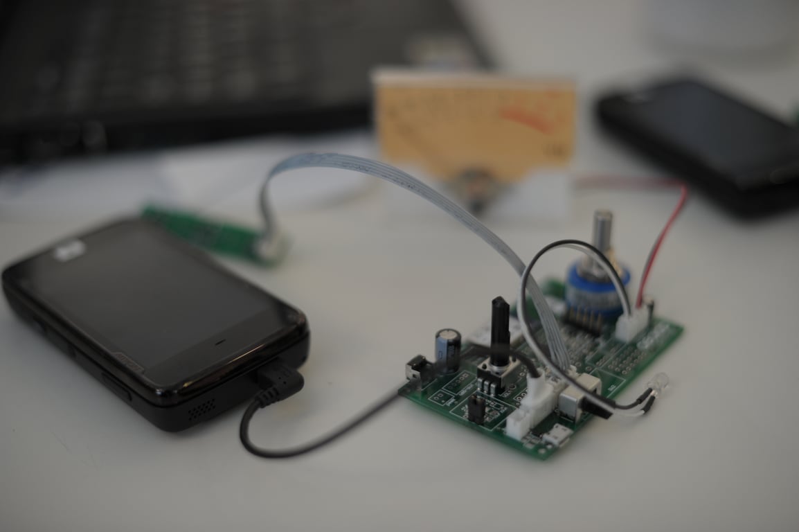 Nokia N900 connected by cables to a green circuit board with a blue rotary control and a separate analog meter.