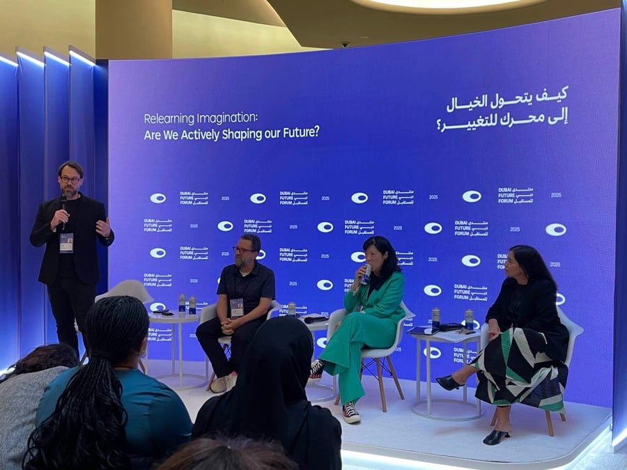 Panel discussion at Dubai Future Forum with four speakers on stage, blue backdrop with text.