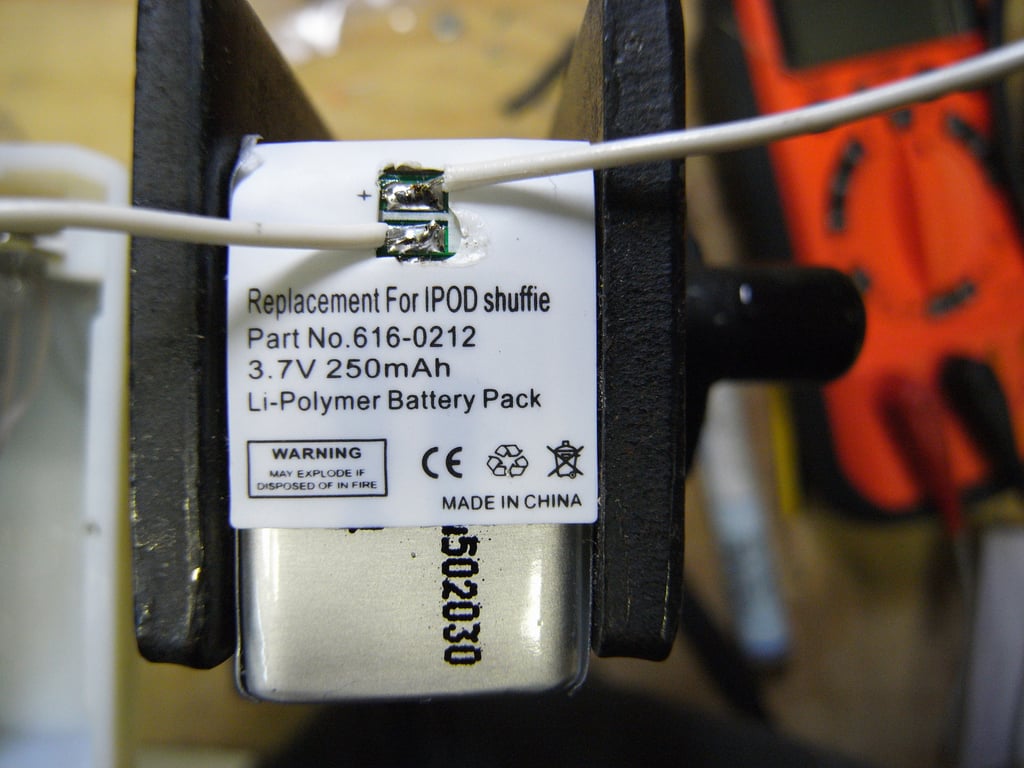A 3.7-volt lithium-polymer battery held in a vise with white wires soldered to its terminals.