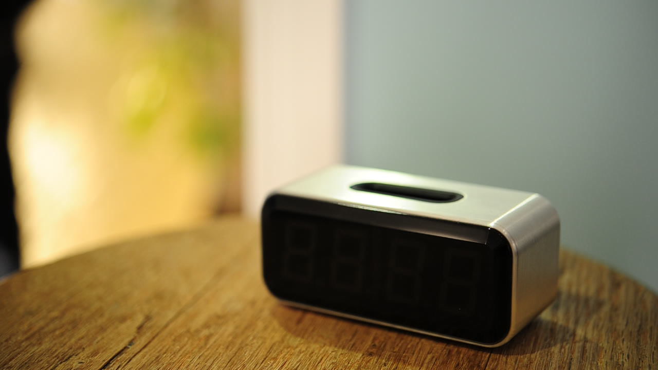 The Social Alarm Clock prototype enclosure rests on a wooden table with its dark display and top phone dock visible.