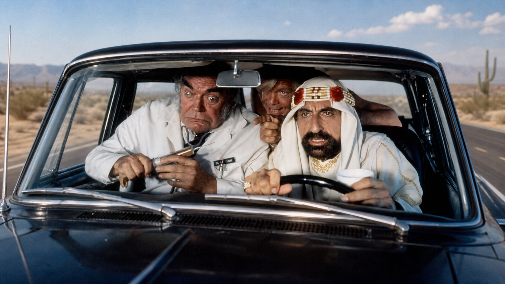 Film still from Cannonball Run showing three men crowded inside a car, with the driver in a white head covering gripping the steering wheel.