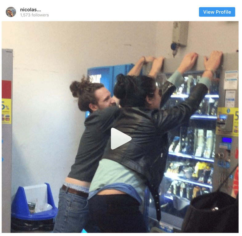 An Instagram video screenshot showing two people reaching over a vending machine, with a play symbol over the image.