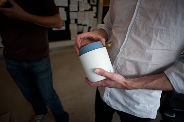 A designer holds a white cylindrical Social Speaker prototype in a workshop.