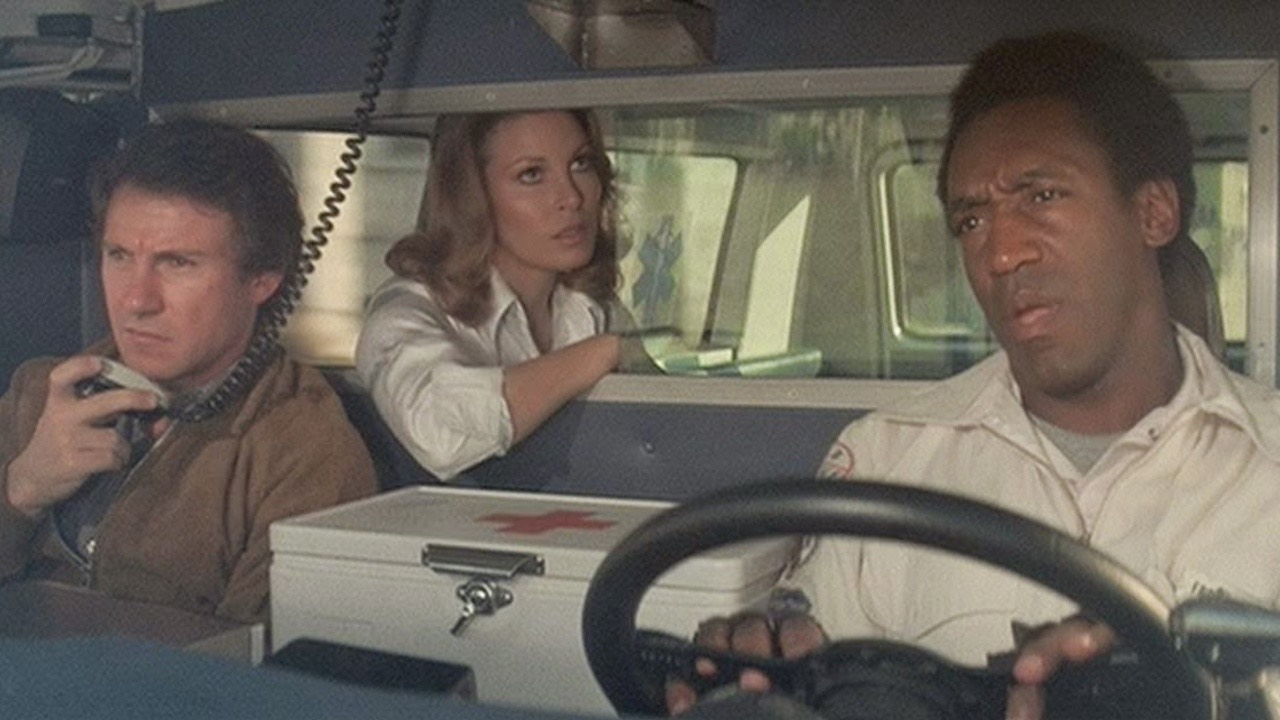 Film still from Mother, Jugs & Speed showing three ambulance-service workers riding in a vehicle.