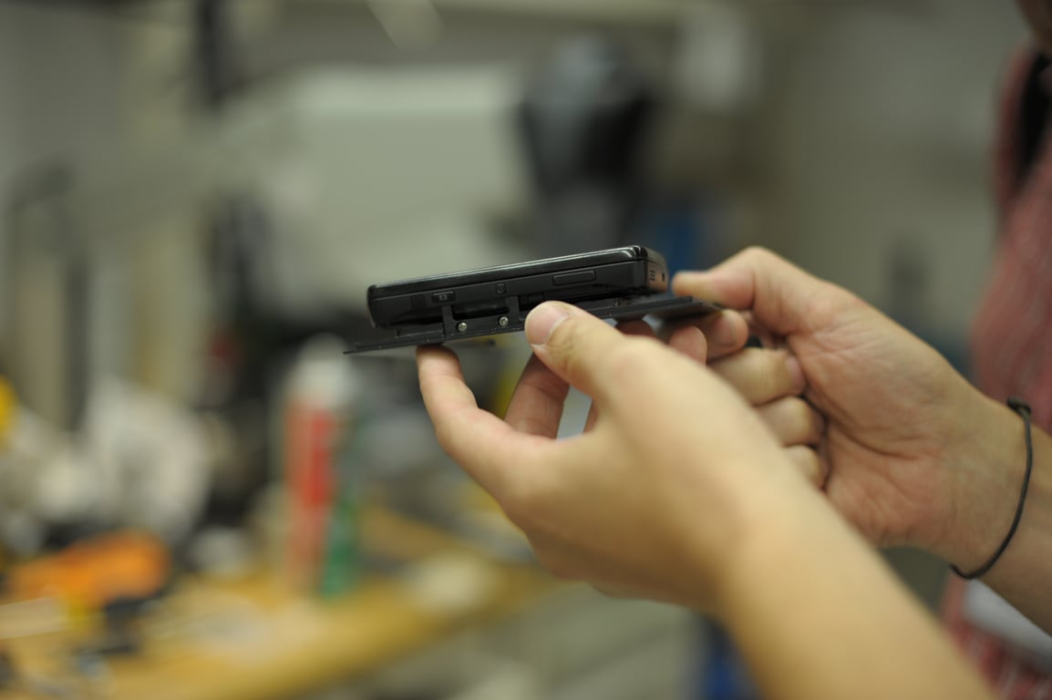 Hands hold a Nokia N900 against a thin mounting plate at the workshop bench.