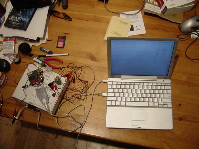 A cluttered desk with a laptop, wires, and electronic components scattered around.