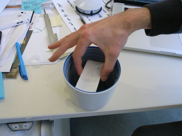 A hand lowers a printed component into a blue-rimmed cylindrical Social Speaker housing.