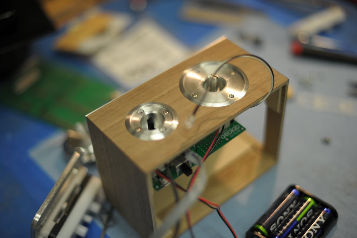 Open wooden Humbo enclosure with circular metal control mounts, visible electronics, and an external battery holder.